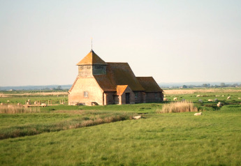 Maison en pierre au toit orange près de New Puddledock Lodge, UK, entourée de moutons dans des champs verts.