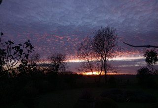 Solnedgang ved New Puddledock Lodge i Storbritannien med dramatiske lilla og orange skyer over træerne.
