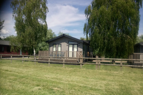 Trælodge ved New Puddledock i Storbritannien, omgivet af grøn græsplæne og høje træer om sommeren.