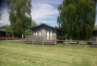 Trælodge ved New Puddledock i Storbritannien, omgivet af grøn græsplæne og høje træer om sommeren.