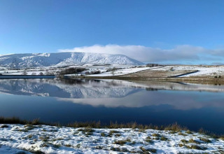 Snedækket landskab ved New Puddledock lodge i Storbritannien med bjerge og sø, der spejler sig.