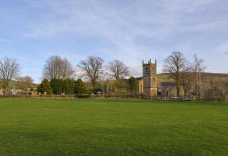 Kirke og grøn mark ved New Puddledock lodge i Storbritannien, omgivet af træer under en blå himmel.