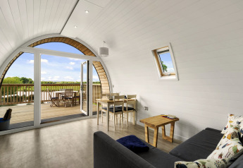 Lichte woonkamer in The Chicken Coop pod met gebogen wand, bank, eettafel en houten terras met uitzicht.
