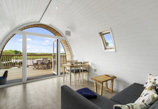 Lichte woonkamer in The Chicken Coop pod met gebogen wand, bank, eettafel en houten terras met uitzicht.