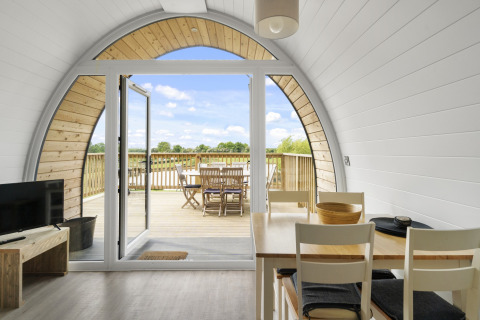 Interieur van een pod met eettafel en glazen deuren naar een houten terras met buitentafel en stoelen.