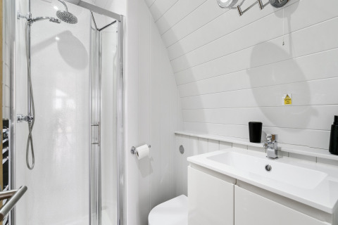 Moderne witte badkamer in The Chicken Coop pod, met douchecabine, wastafel en zwartkleurige accessoires.