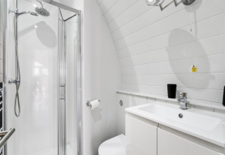Moderne witte badkamer in The Chicken Coop pod, met douchecabine, wastafel en zwartkleurige accessoires.