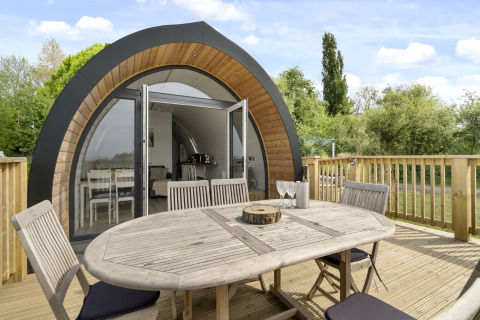 Houten tafel en stoelen op het terras voor de gebogen houten pod The Chicken Coop met glazen voordeur.