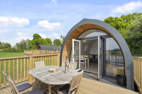 Buitenterras met houten eettafel bij glampingpod The Chicken Coop, op het platteland van het Verenigd Koninkrijk.