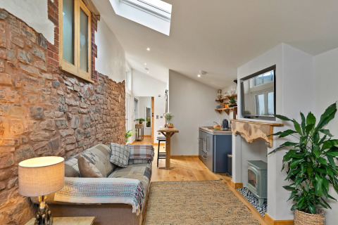 Stilfuld stue med synlig naturstensvæg, hyggelig sofa og moderne køkken i Hillfarrow Hideaway, Storbritannien.