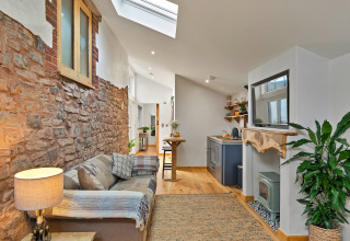 Stilfuld stue med synlig naturstensvæg, hyggelig sofa og moderne køkken i Hillfarrow Hideaway, Storbritannien.