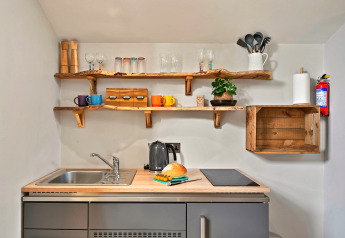 Piccola cucina al Hillfarrow Hideaway, UK, con mensole in legno, lavello, bollitore e pagnotta.