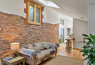 Lys stue i Hillfarrow Hideaway med stenvæg, hyggelig sofa og træborde, naturligt britisk interiør.