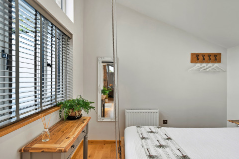 Lyst og moderne soveværelse med stort vindue, træbord, plante og spejl i Hillfarrow Hideaway, UK.