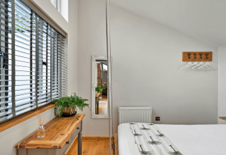 Lyst og moderne soveværelse med stort vindue, træbord, plante og spejl i Hillfarrow Hideaway, UK.