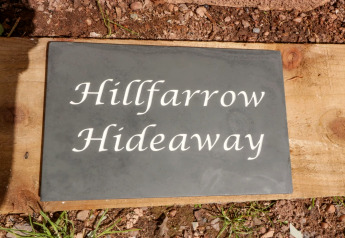 Un'insegna con scritto 'Hillfarrow Hideaway' fuori da una baita nel Regno Unito, su legno e terra.