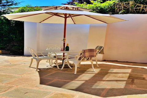 Udendørs terrasse ved Hillfarrow Hideaway, England, med stole, bord, parasol og solskin.