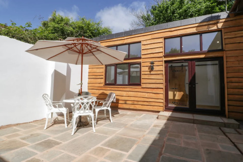 Udendørs terrasse ved Hillfarrow Hideaway med træbeklædt facade, havesæt og stor parasol.
