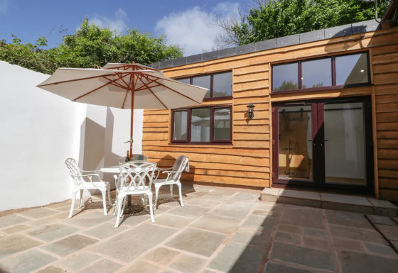 Udendørs terrasse ved Hillfarrow Hideaway med træbeklædt facade, havesæt og stor parasol.