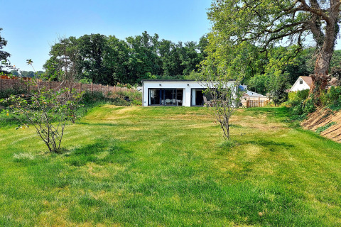 Billede af Little Dunley - Apple Lodge med grøn græsplæne, små træer og moderne hytte i baggrunden.