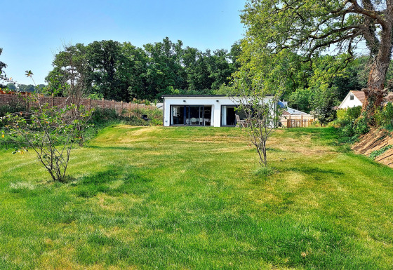 Billede af Little Dunley - Apple Lodge med grøn græsplæne, små træer og moderne hytte i baggrunden.
