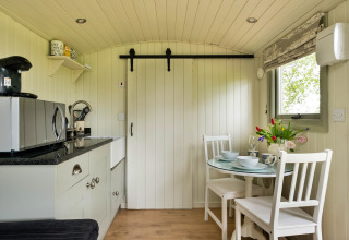 Angolo cucina e zona pranzo accoglienti nella cabina Hay and Hedgerow Glamping con comfort moderni nel Regno Unito.
