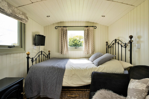 Accogliente camera di una cabina con letto in ferro e finestre, Hay and Hedgerow Glamping, Regno Unito.