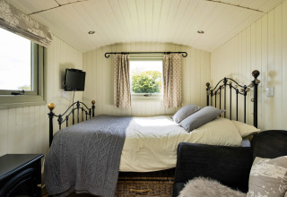 Accogliente camera di una cabina con letto in ferro e finestre, Hay and Hedgerow Glamping, Regno Unito.