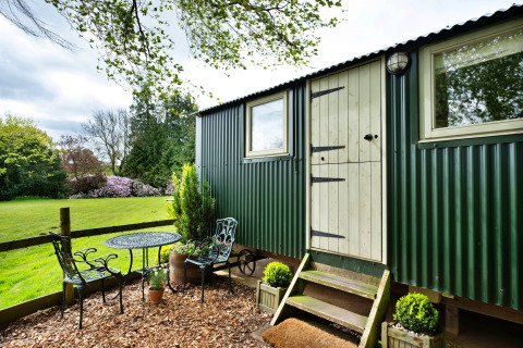 Area esterna con tavolo e sedie vicino a una cabina verde da Hay and Hedgerow Glamping nel Regno Unito.