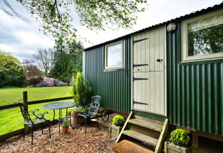 Area esterna con tavolo e sedie vicino a una cabina verde da Hay and Hedgerow Glamping nel Regno Unito.
