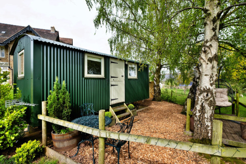 Cabina verde all'Hay and Hedgerow Glamping nel Regno Unito, immersa nel verde, area relax esterna visibile.