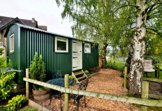 Cabina verde all'Hay and Hedgerow Glamping nel Regno Unito, immersa nel verde, area relax esterna visibile.