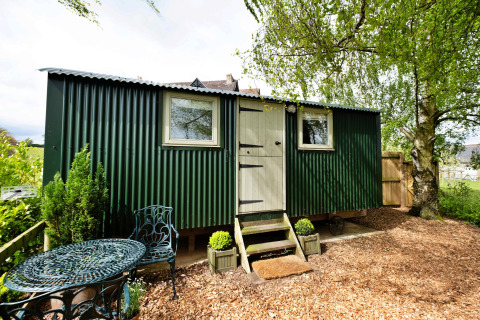 Piccola casa verde in lamiera ondulata con arredamento da giardino presso Hay and Hedgerow Glamping nel Regno Unito.