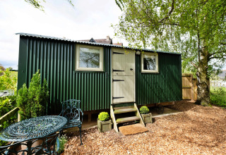 Piccola casa verde in lamiera ondulata con arredamento da giardino presso Hay and Hedgerow Glamping nel Regno Unito.