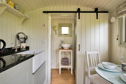 Interno della cabina Hay and Hedgerow Glamping nel Regno Unito con cucina, tavolo da pranzo e bagno.