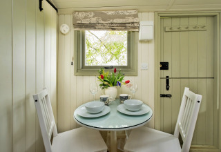 Accogliente angolo pranzo in una cabina con tavolo tondo, due sedie bianche e vista sul verde.