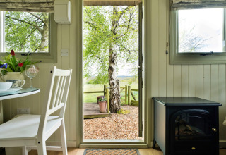 Interno di una cabina accogliente con porta aperta e vista sull’albero e campagna a Hay and Hedgerow Glamping UK