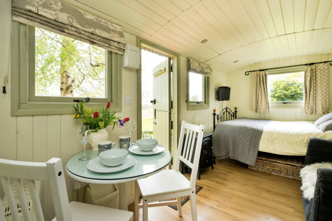 Interno di una luminosa cabina glamping a Hay and Hedgerow, Regno Unito, con tavolo, letto e finestre.