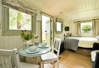 Interno di una luminosa cabina glamping a Hay and Hedgerow, Regno Unito, con tavolo, letto e finestre.