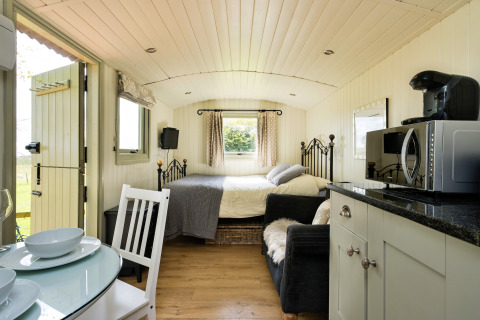 Interno luminoso della cabina Hay and Hedgerow Glamping con letto, cucina, divano e tavolo da pranzo.