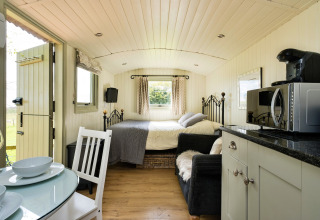 Interno luminoso della cabina Hay and Hedgerow Glamping con letto, cucina, divano e tavolo da pranzo.