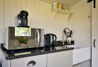Angolo cottura luminoso con microonde, macchina del caffè, bollitore e lavello in Hay and Hedgerow Glamping, UK.