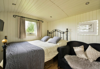 Camera accogliente in una cabina con letto matrimoniale, divano e finestra a Hay and Hedgerow Glamping, Regno Unito.