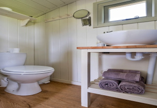 Bagno moderno con wc bianco, lavabo su ripiano in legno e asciugamani viola arrotolati sulla mensola sotto.