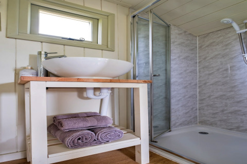 Bagno moderno presso Hay and Hedgerow Glamping nel Regno Unito, con lavabo, asciugamani e box doccia vetrato.