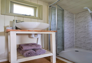 Bagno moderno presso Hay and Hedgerow Glamping nel Regno Unito, con lavabo, asciugamani e box doccia vetrato.