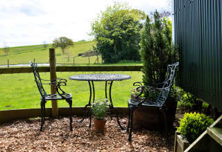 Tavolo e due sedie nere in metallo all’aperto con vista sui prati verdi di Hay and Hedgerow Glamping, Regno Unito.