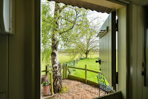Vista da una cabina presso Hay and Hedgerow Glamping su campi verdi e alberi nel Regno Unito.