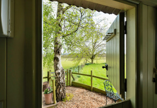 Vista da una cabina presso Hay and Hedgerow Glamping su campi verdi e alberi nel Regno Unito.