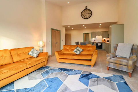 Woonkamer in Little Rissington - Barn Four met gele zetels, grote wandklok en modern blauw tapijt.
